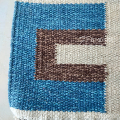 Textile art piece with blue, brown, and white pattern on a plain background