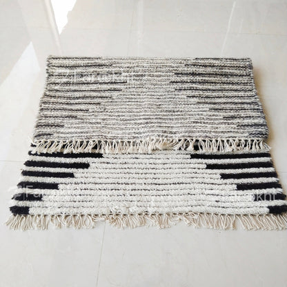 Black and white striped rug with fringes on a light gray floor.