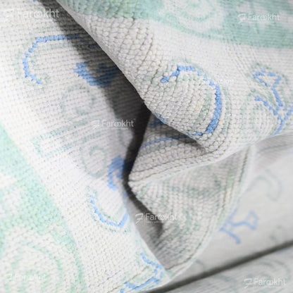 Close-up of a textured fabric with blue and green patterns, branded &