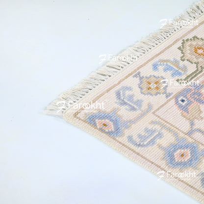 Decorative rug with floral patterns and fringe on a light blue background, branded &